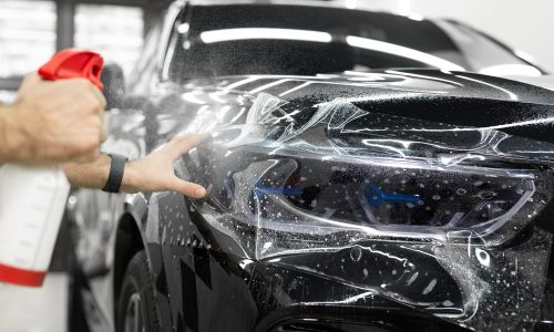 Worker applies a protective film or anti-gravity protective coating to the car headlight. Details of the car