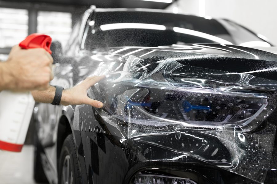 Worker applies a protective film or anti-gravity protective coating to the car headlight. Details of the car